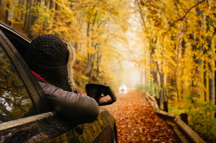 Hombre asomándose por la ventanilla de su todoterreno en una carretera de otoño
