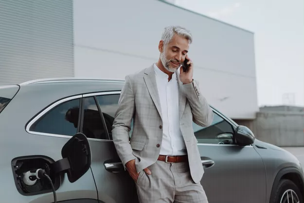 hombre hablando por teléfono mientras carga su coche eléctrico